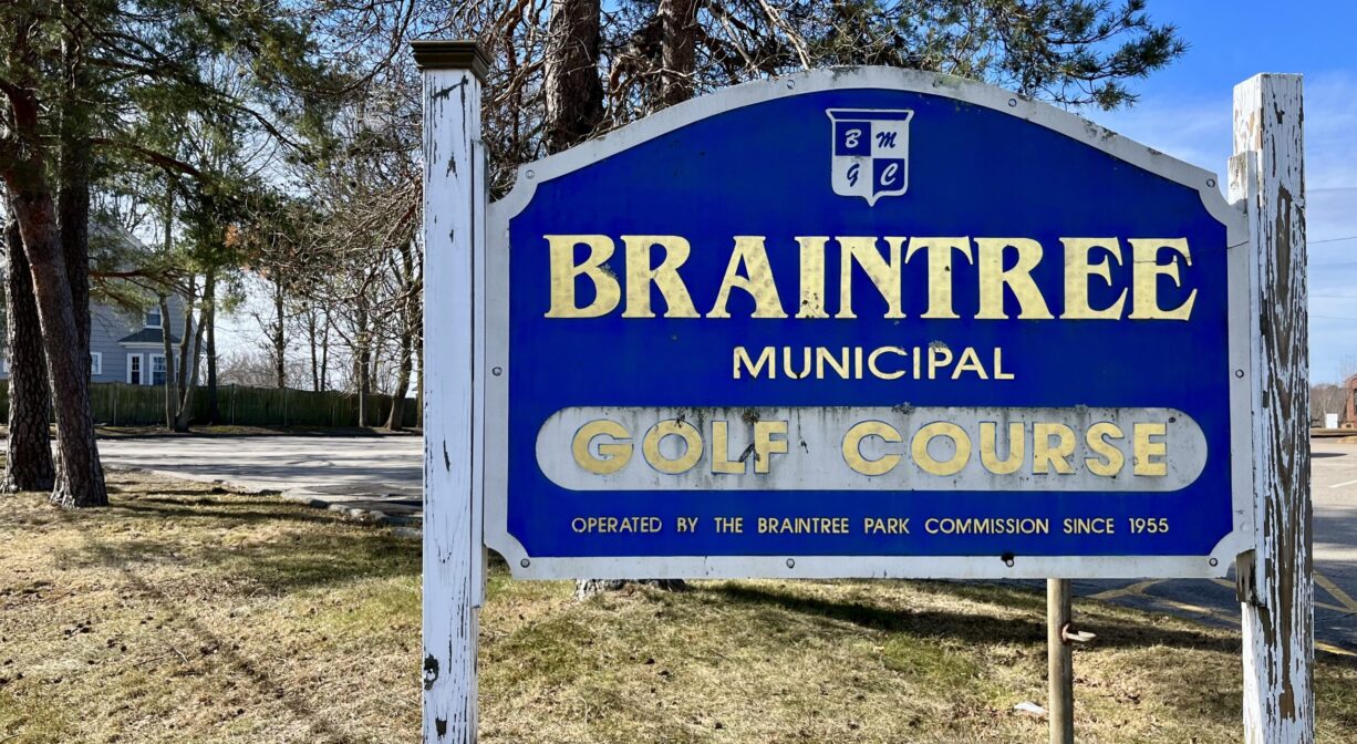 A photograph of a property sign with grass and trees