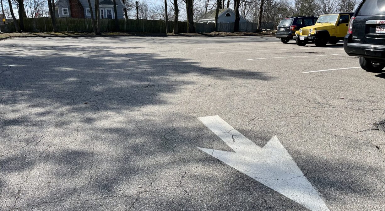 A photograph of a paved parking area with a large white arrow.