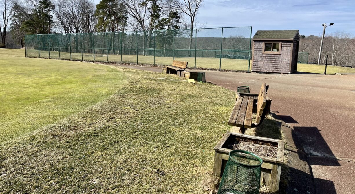 A photograph of a green on a golf course with a bench and a paved path to one side.